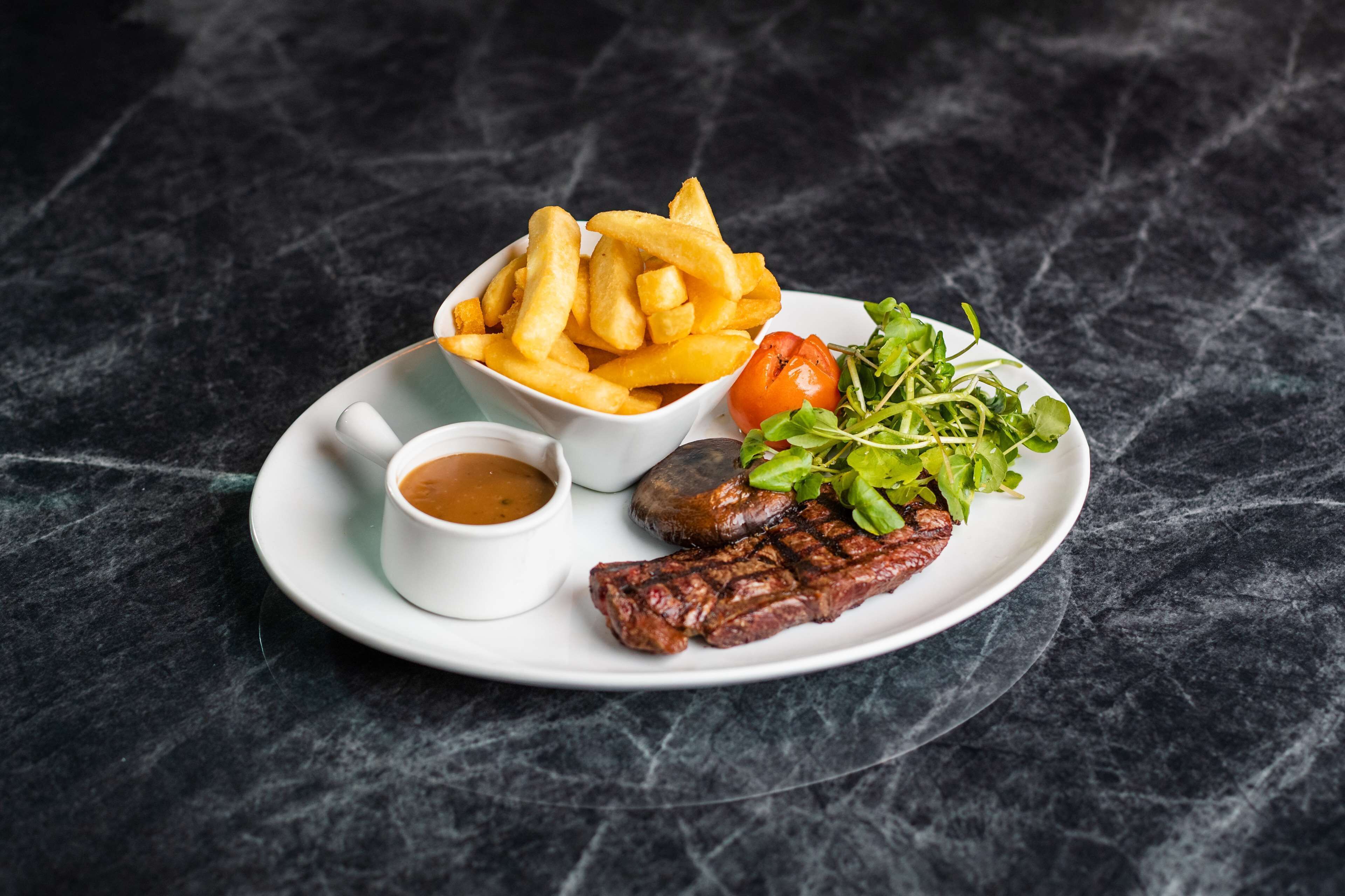 A plate with steak, fries, a small salad, and a cup of sauce.