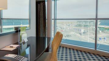 A hotel room with a large window offering a view of an airport.