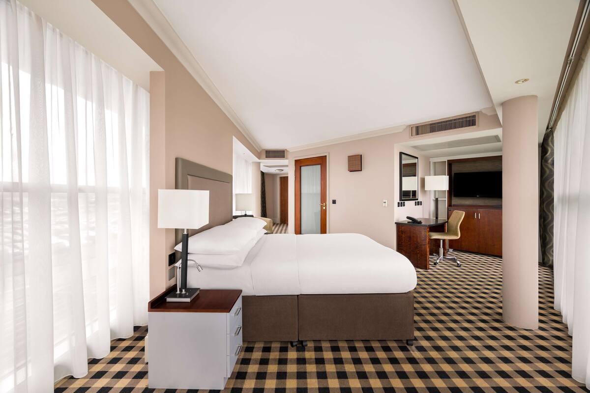 A hotel room with a bed, bedside table, lamp, and a checkered floor.