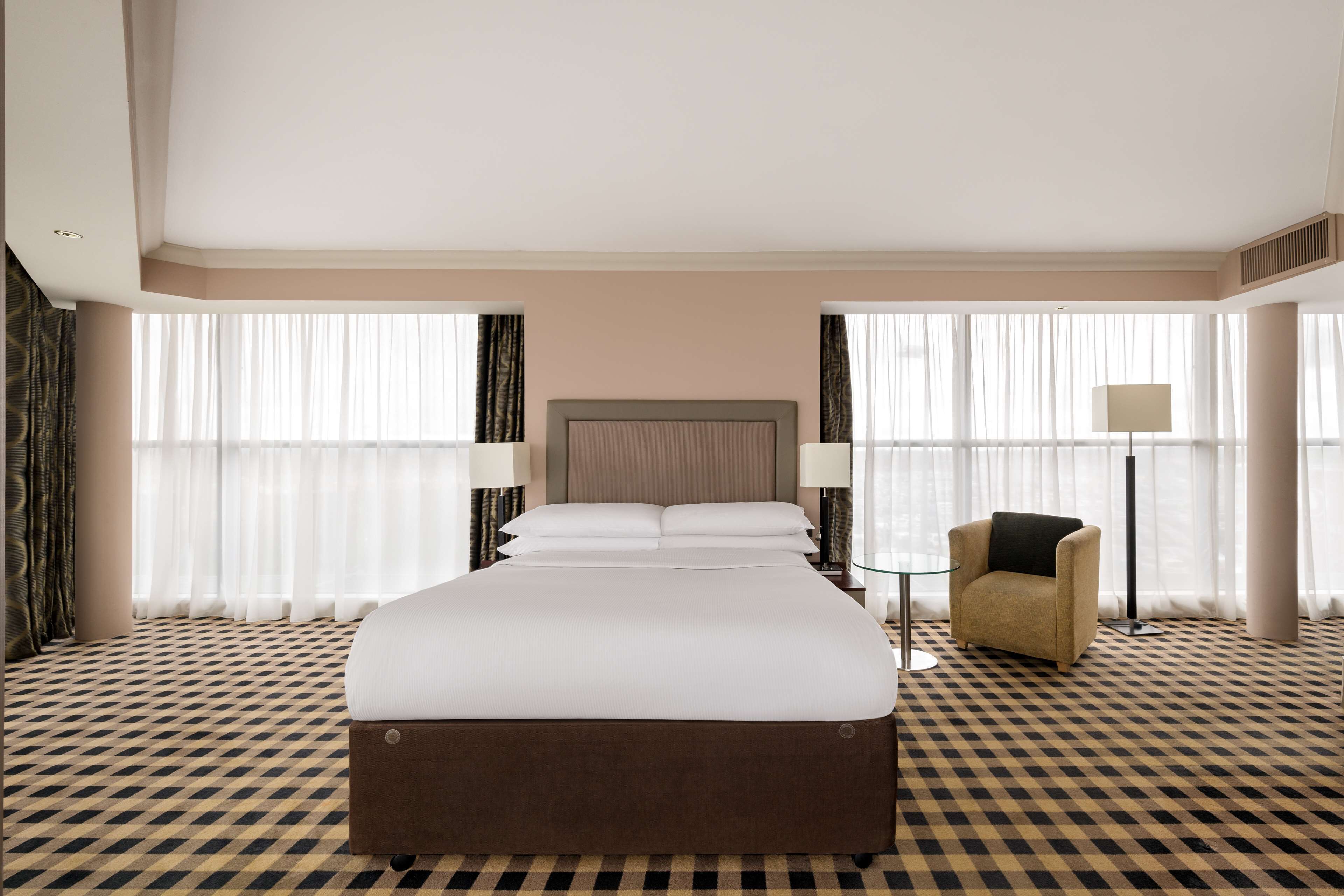 A hotel room with a large bed, a chair, and a lamp.