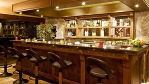 A bar area with wooden bar stools, a countertop with bottles, and a stone wall backdrop. - Padok Premium Hotel and Stables (Ula)