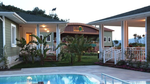 A hotel with a swimming pool, outdoor seating, and a covered patio area. - Padok Premium Hotel and Stables (Ula)
