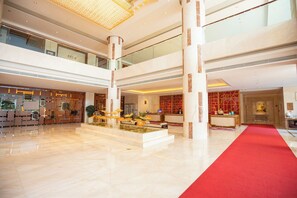 Un vestíbulo amplio con alfombra roja, una recepción y un elemento decorativo de agua.
