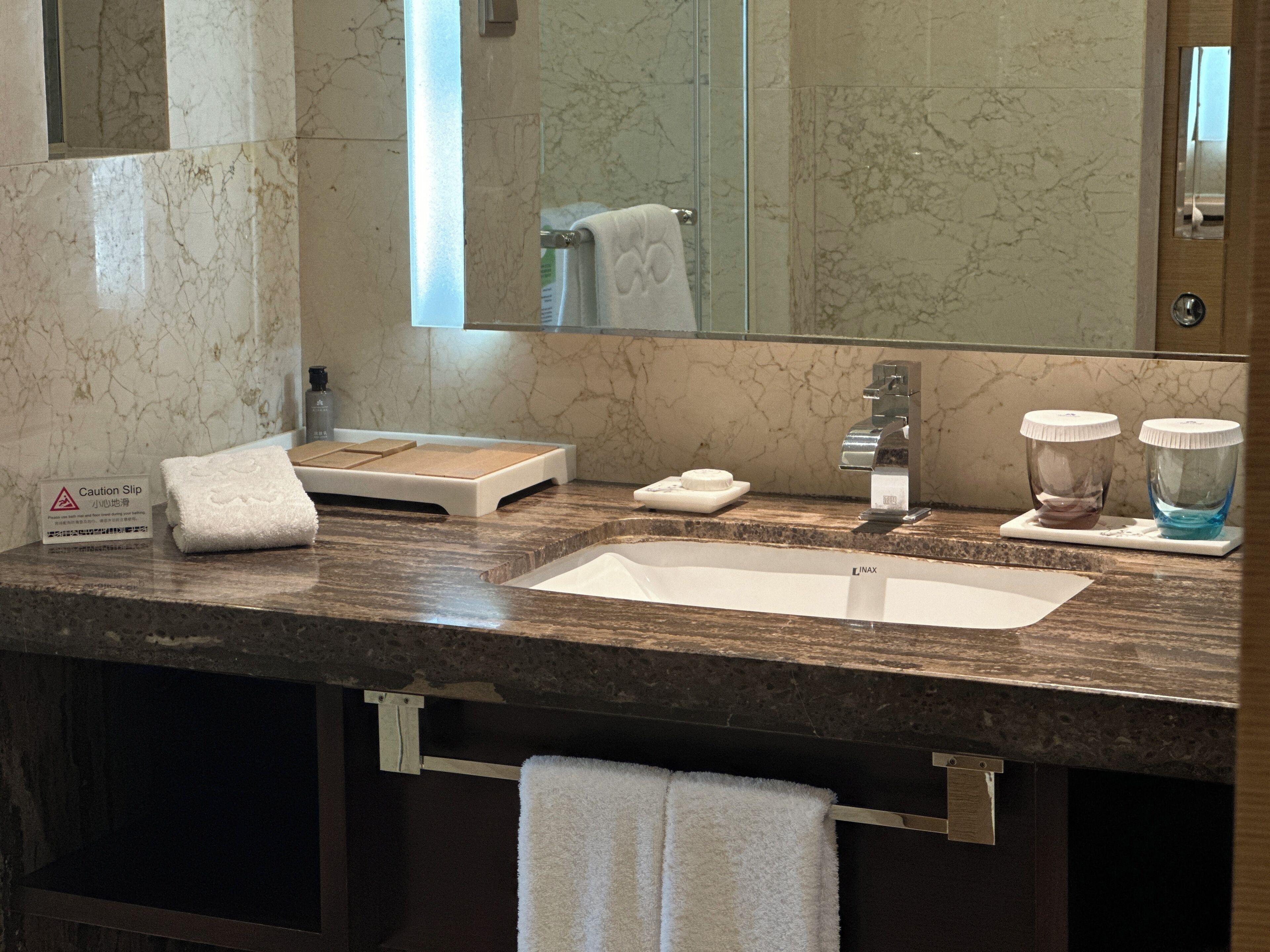A bathroom with a marble sink, a towel rack, a caution slip sign, and a mirror.