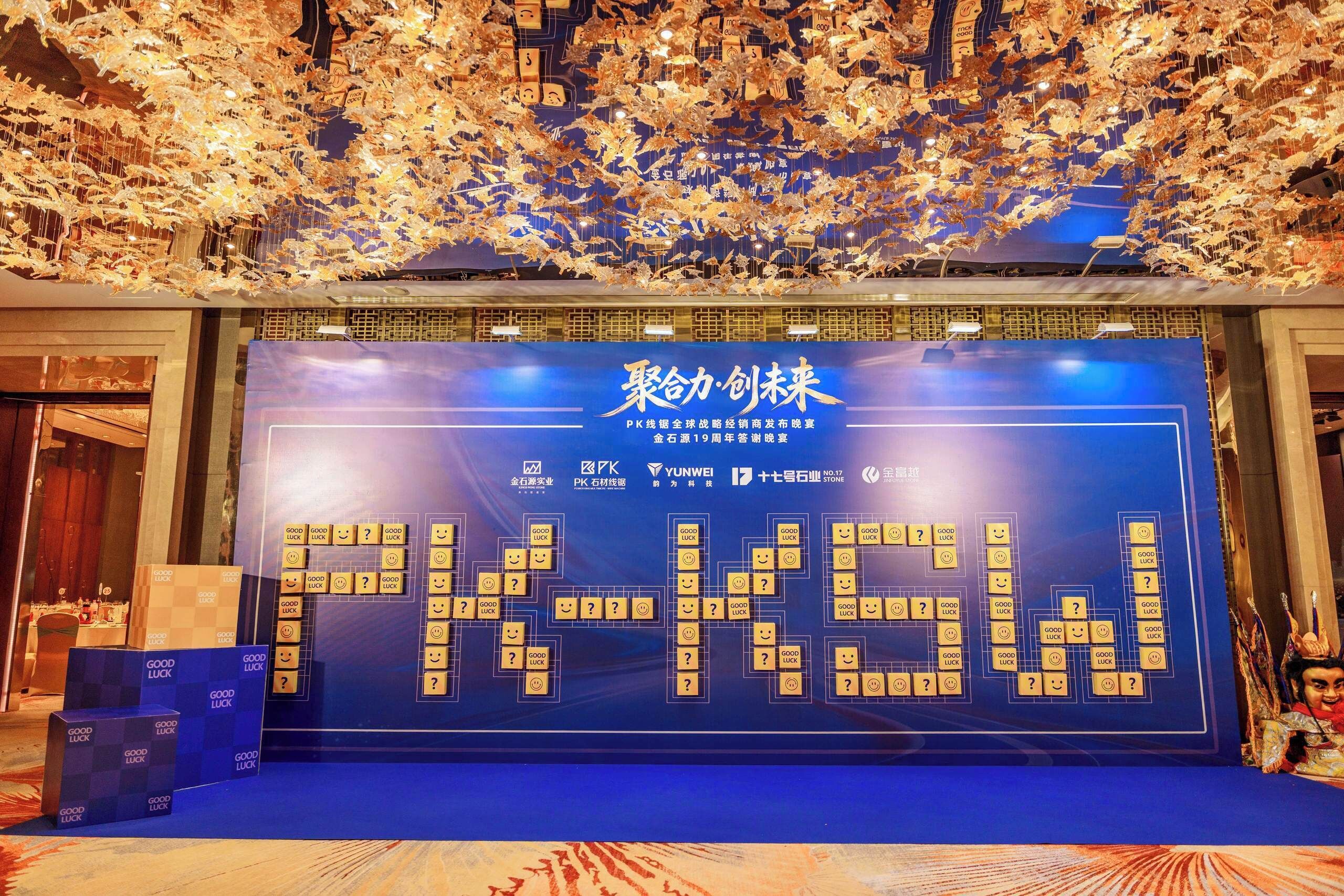 A stage with a large display board featuring a grid of icons and text, a ceiling with hanging decorations, and a podium with a blue backdrop.