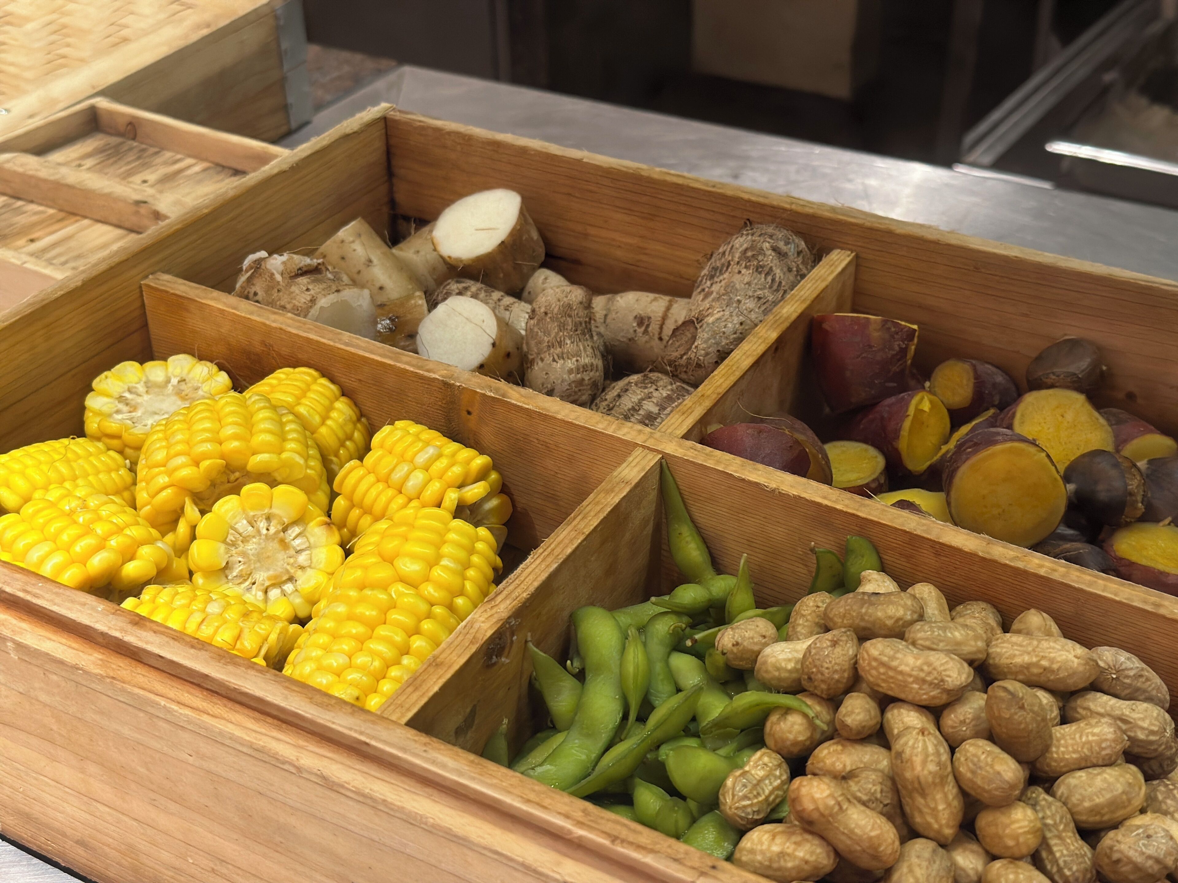 Wooden crates with various food items including corn, green beans, and peanuts.