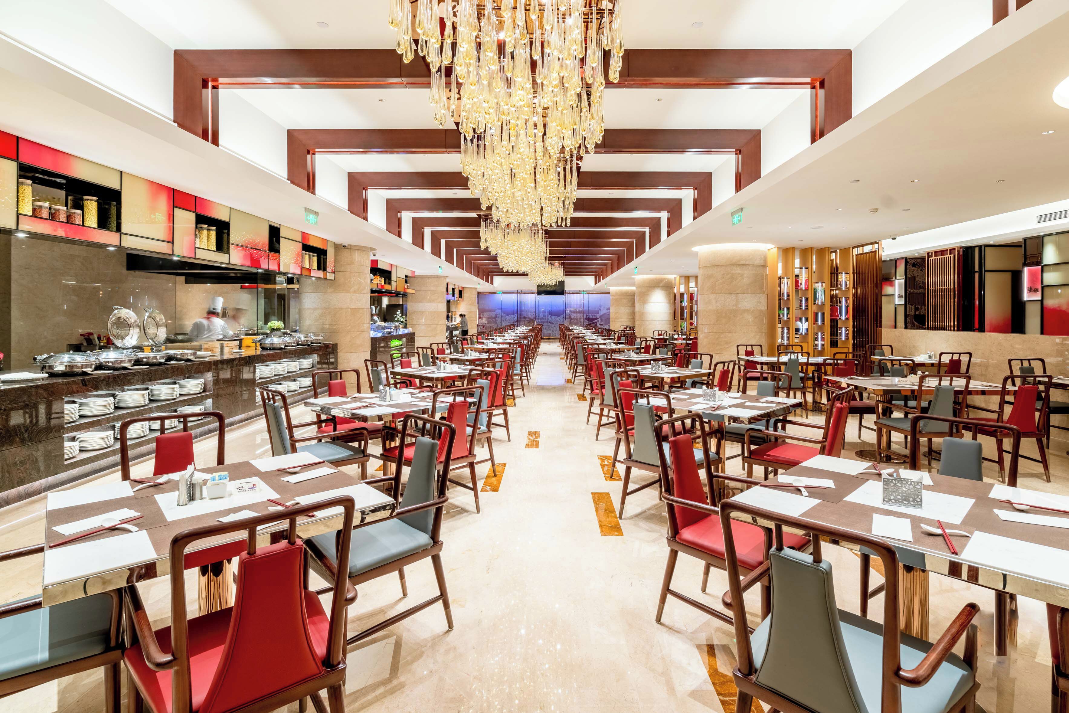 Uma sala de jantar espaçosa, com várias mesas e cadeiras, um lustre central e um design de interiores moderno.