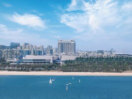 Un paisaje urbano costero con modernos rascacielos, una playa de arena y veleros en el agua.