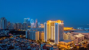 Un hotel de gran altura con varios pisos, una entrada destacada y vistas de la ciudad iluminada de noche.