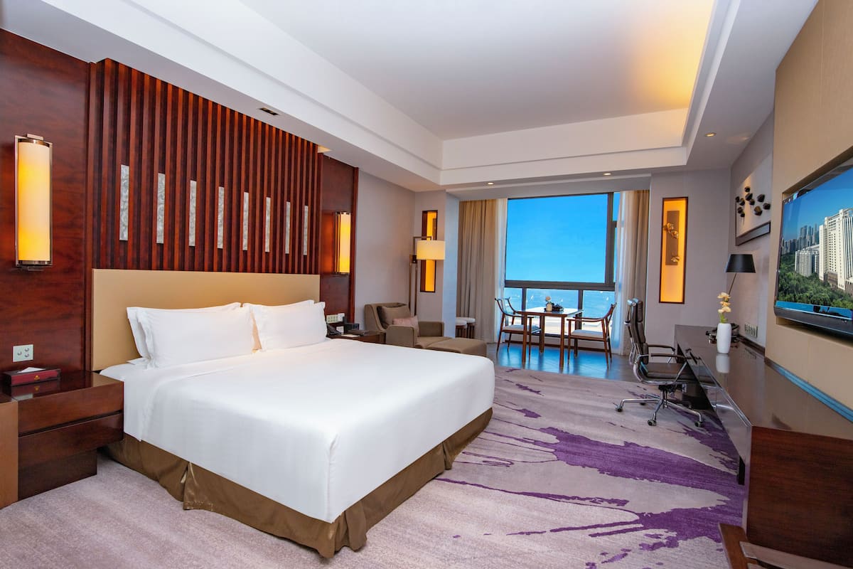 Habitación de hotel con una cama grande, un escritorio, una silla, un televisor y un balcón con vistas.