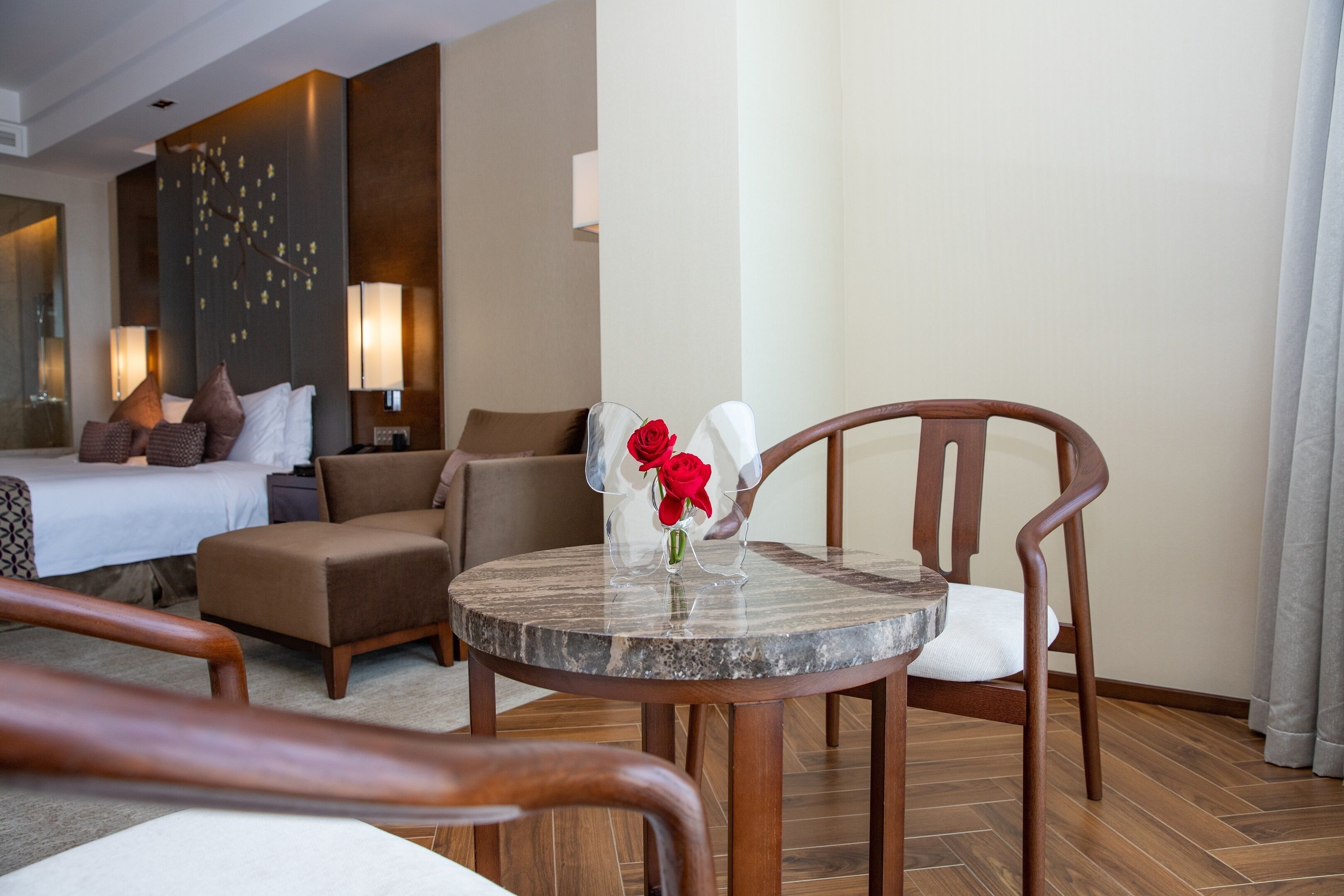 A hotel room with a bed, a sitting area with a table and chairs, and a decorative vase with flowers.