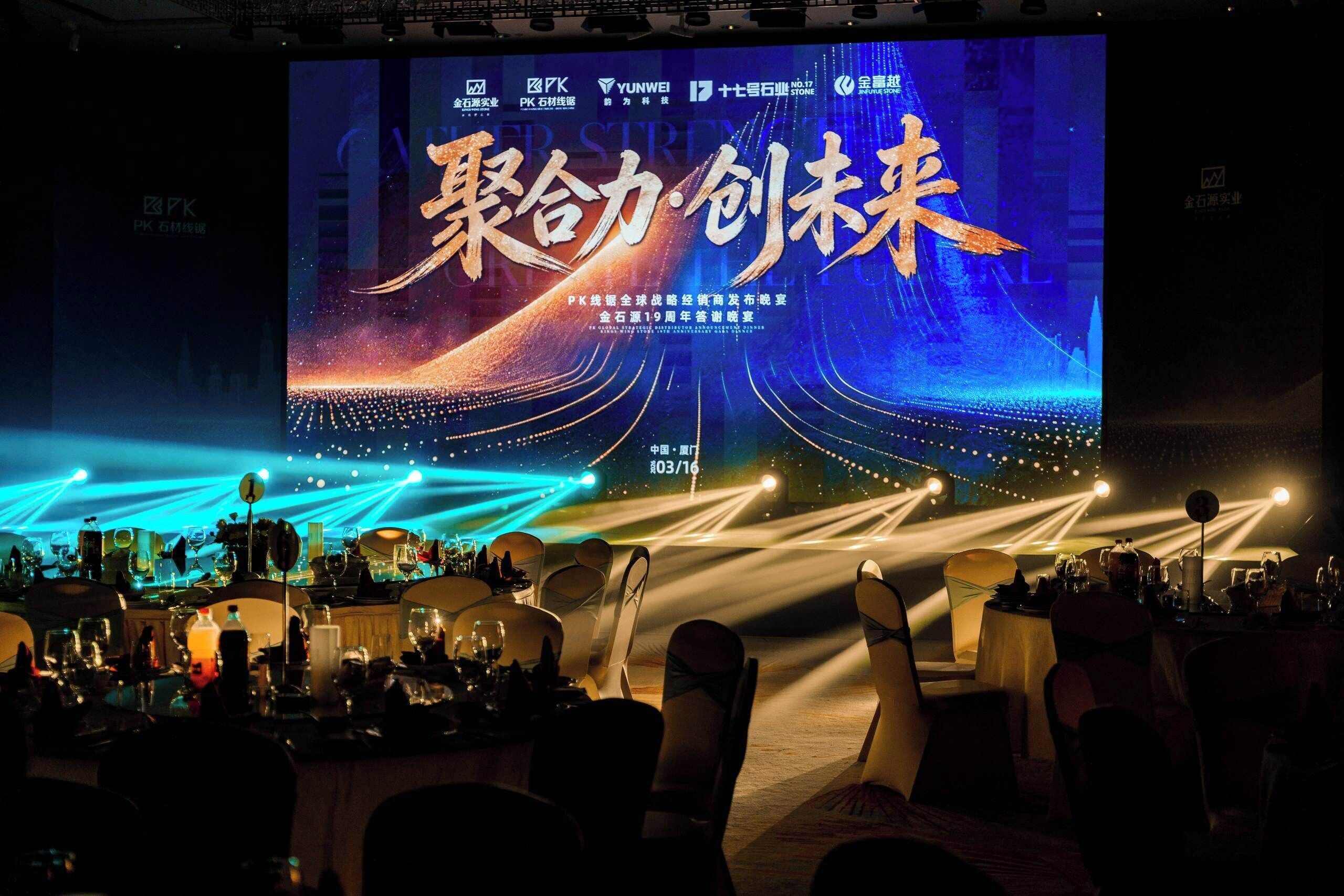 A stage with a large screen displaying text and a date, surrounded by tables and chairs.