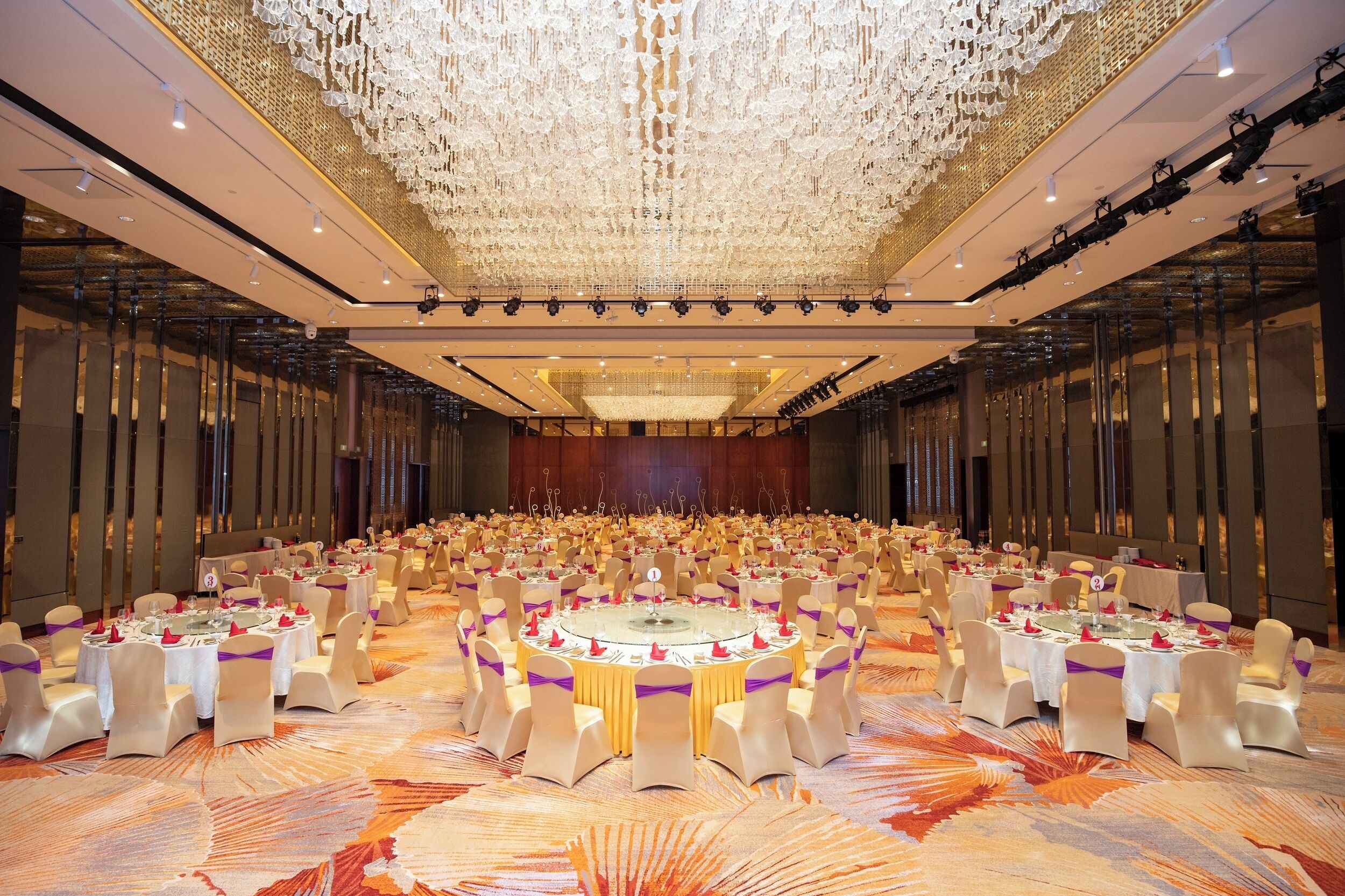 A large banquet hall with round tables, white chairs, and a decorative ceiling.
