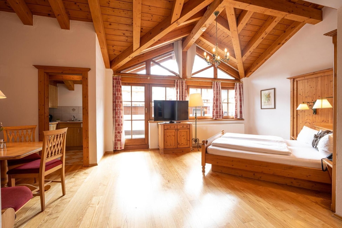 Une pièce avec un plafond en bois, un lit, une télévision, un bureau et une fenêtre avec des rideaux.