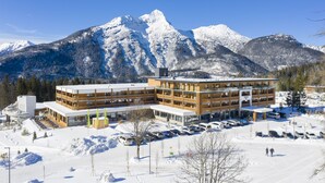 A modern hotel with multiple floors, a parking lot, and a view of snow-covered mountains.