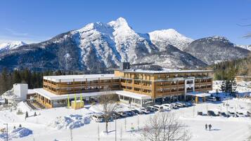 A modern hotel with multiple floors, a parking lot, and a view of snow-covered mountains.