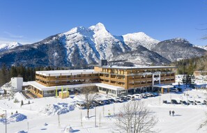 A modern hotel with multiple floors, a parking lot, and a view of snow-covered mountains. - Zugspitz Resort (Ehrwald)