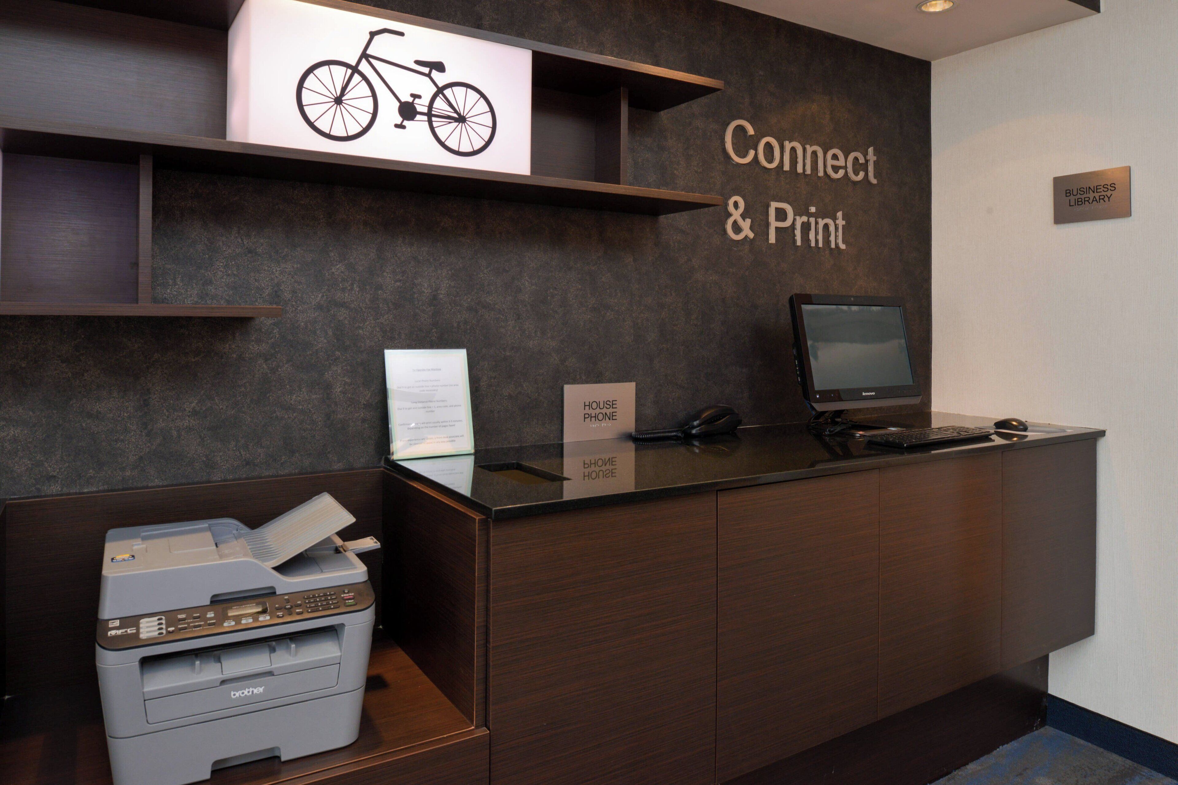 A reception desk with a printer, a computer monitor, and a sign that reads "Connect & Print."