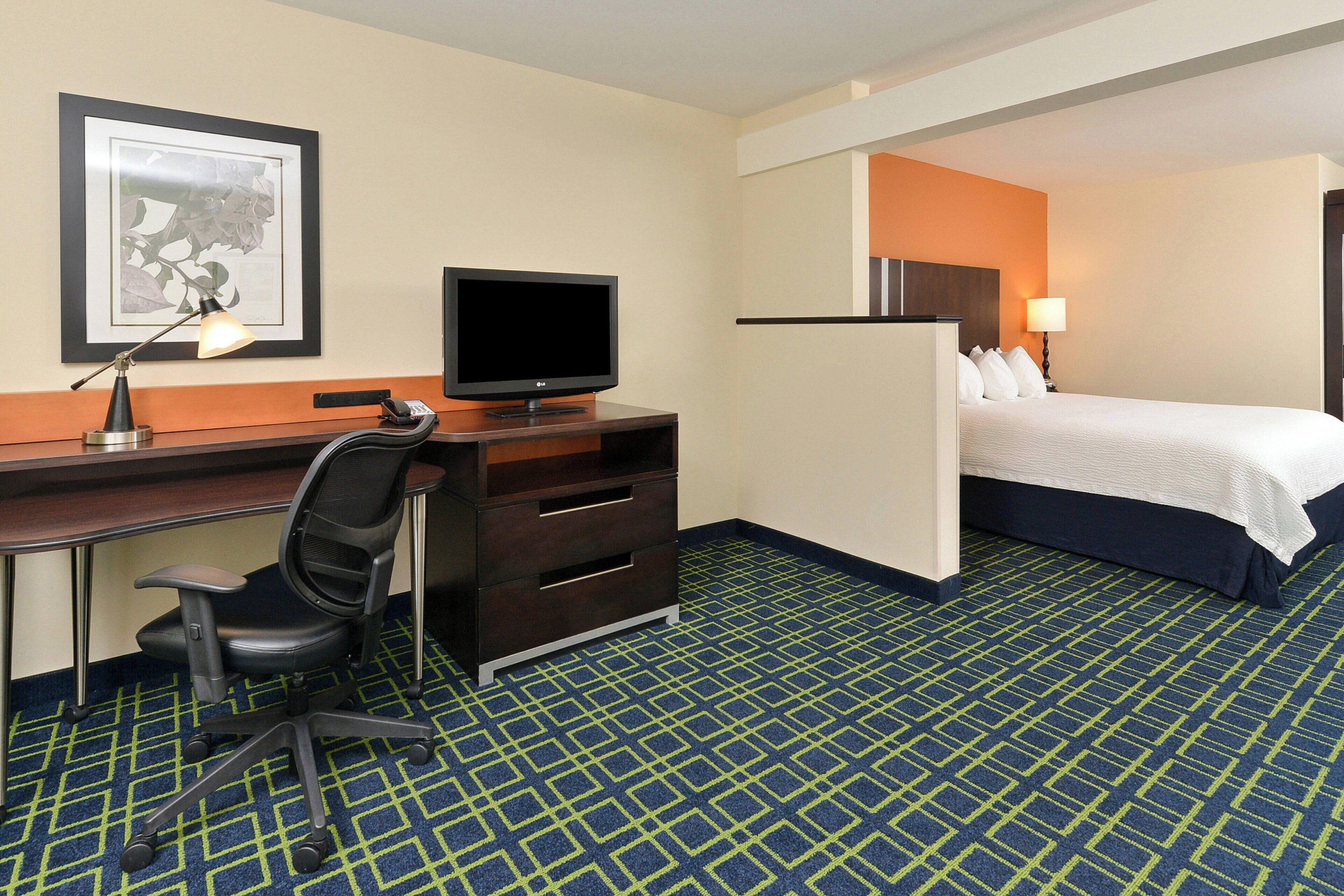 A hotel room with a desk, chair, television, bed, and a framed picture on the wall.