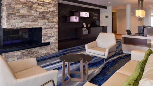 A modern lobby with a stone fireplace, a reception desk, and seating areas. - Fairfield Inn & Suites Cedar Rapids (Cedar Rapids)