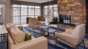A hotel lobby with a stone fireplace, comfortable seating, large windows, and a flat-screen TV. - Fairfield Inn & Suites Cedar Rapids (Cedar Rapids)