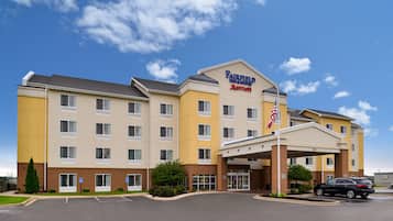 A Fairfield Inn & Suites by Marriott hotel with a central entrance, parking lot, and a clear blue sky.