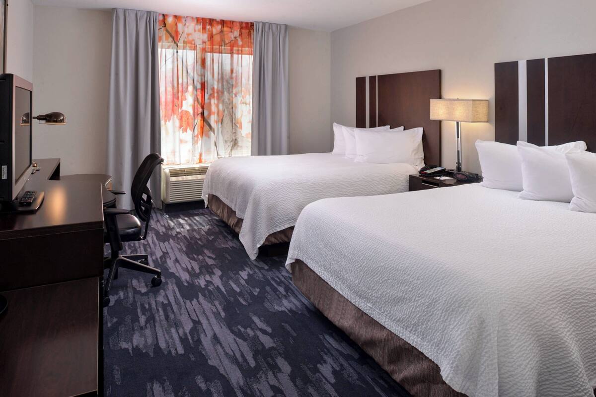 A hotel room with two beds, a desk with a computer, a chair, and a window with curtains.