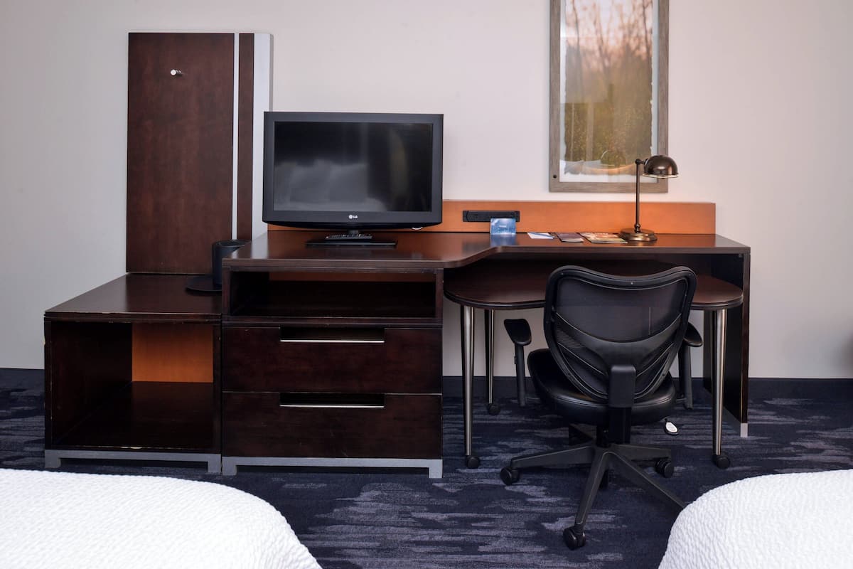 Una habitación de hotel con un escritorio de madera, televisor, una silla y una cama.