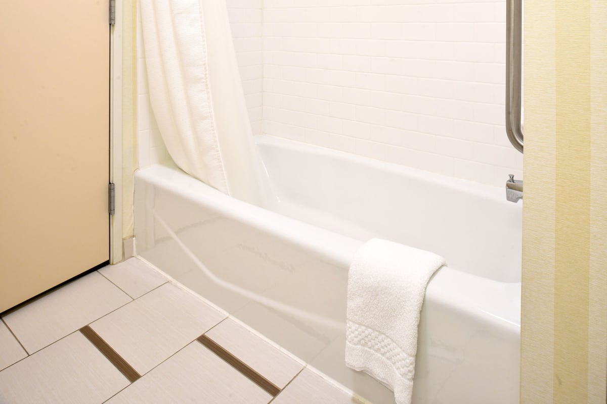 Un baño con una bañera blanca, una cortina de ducha blanca y una toalla blanca colgada de la bañera.