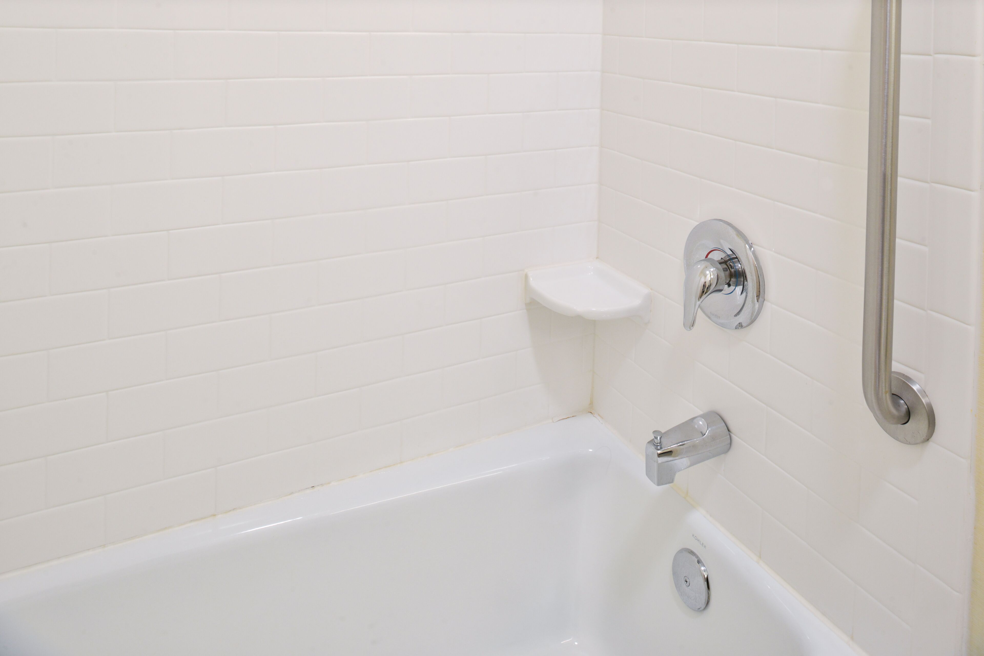 A white bathtub with chrome fixtures, a small shelf, and a wall-mounted mirror.