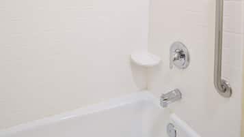 A white bathtub with chrome fixtures, a small shelf, and a wall-mounted mirror.