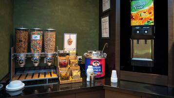 Una barra de desayuno con varios dispensadores de alimentos, un dispensador de jugo y un recipiente de avena Quaker.