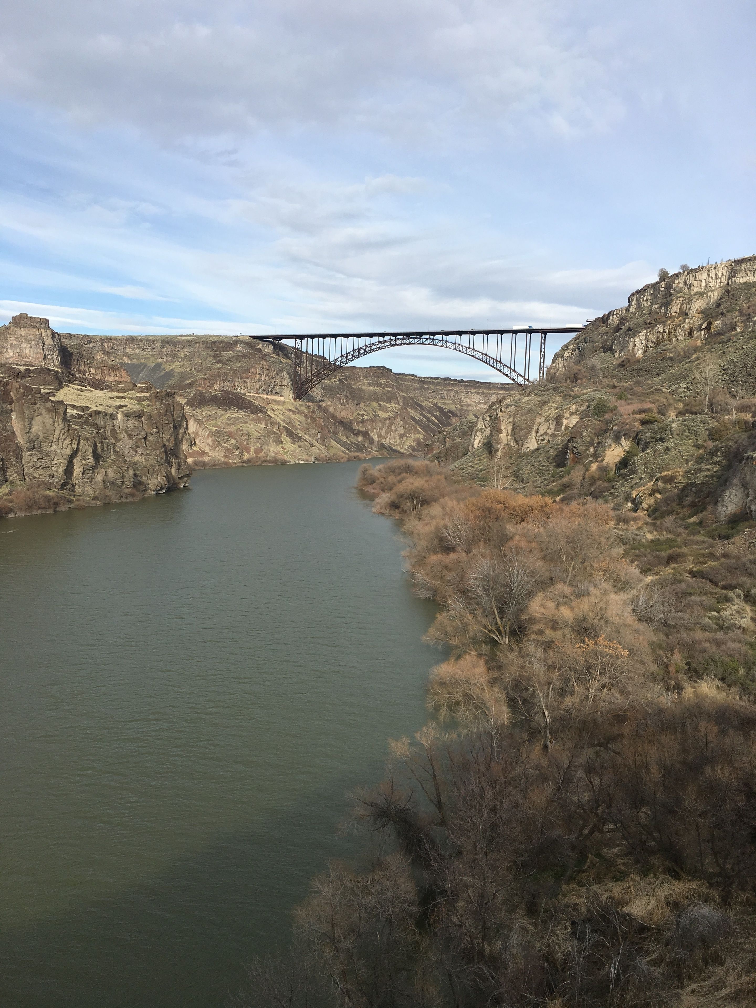 A river with a bridge spanning across it, surrounded by rocky terrain and sparse vegetation.
