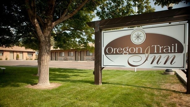 A sign for Oregon Trail Inn with a tree and building in the background. - Oregon Trail Inn (Buhl)