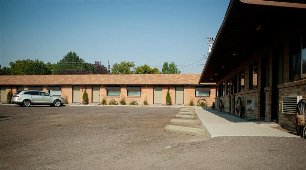 A motel with a parking lot, a single-story building, and a row of rooms with windows.