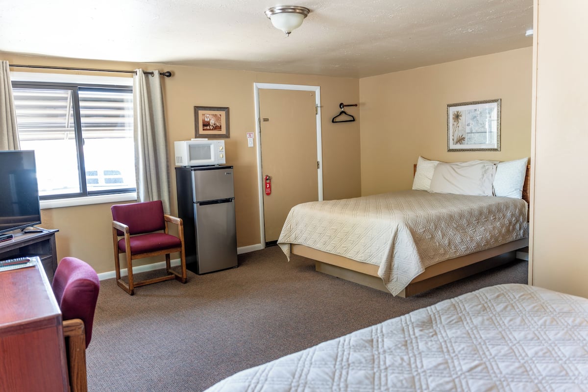 Quarto de hotel com cama, escrivaninha com computador, cadeira, frigorífico e televisão.