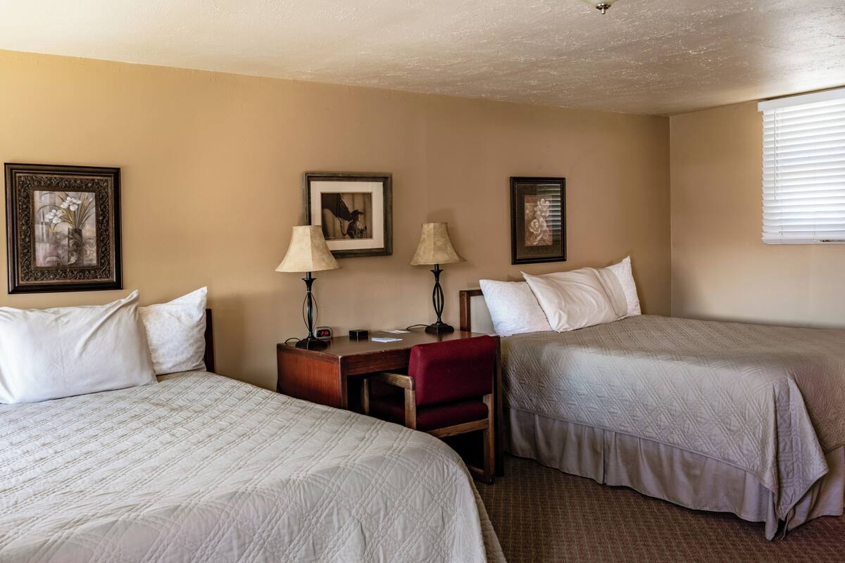 A hotel room with two beds, a desk with a chair, and framed pictures on the wall.
