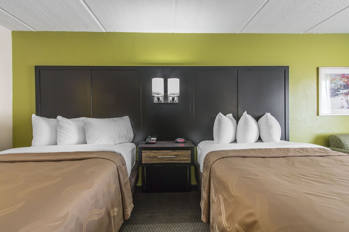 A hotel room with two beds, a nightstand, and a wall-mounted light fixture.