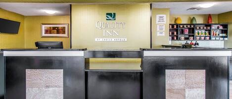 Una recepción con un letrero que dice "Quality Inn by Choice Hotels", un televisor de pantalla plana y un estante con diversos objetos.