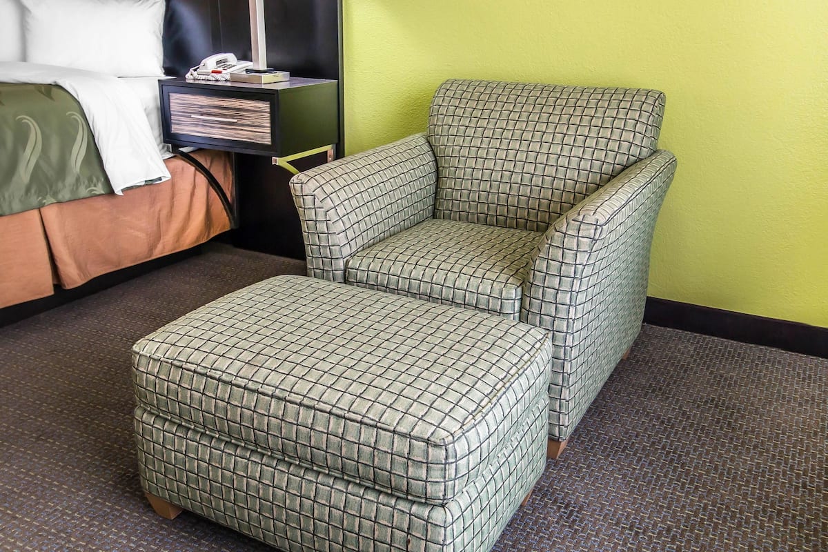 A checkered armchair and ottoman in a hotel room with a bed, a nightstand, and a green wall.