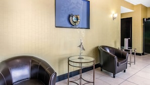 A lobby with two leather armchairs, a glass table, a framed artwork, and a reception area.