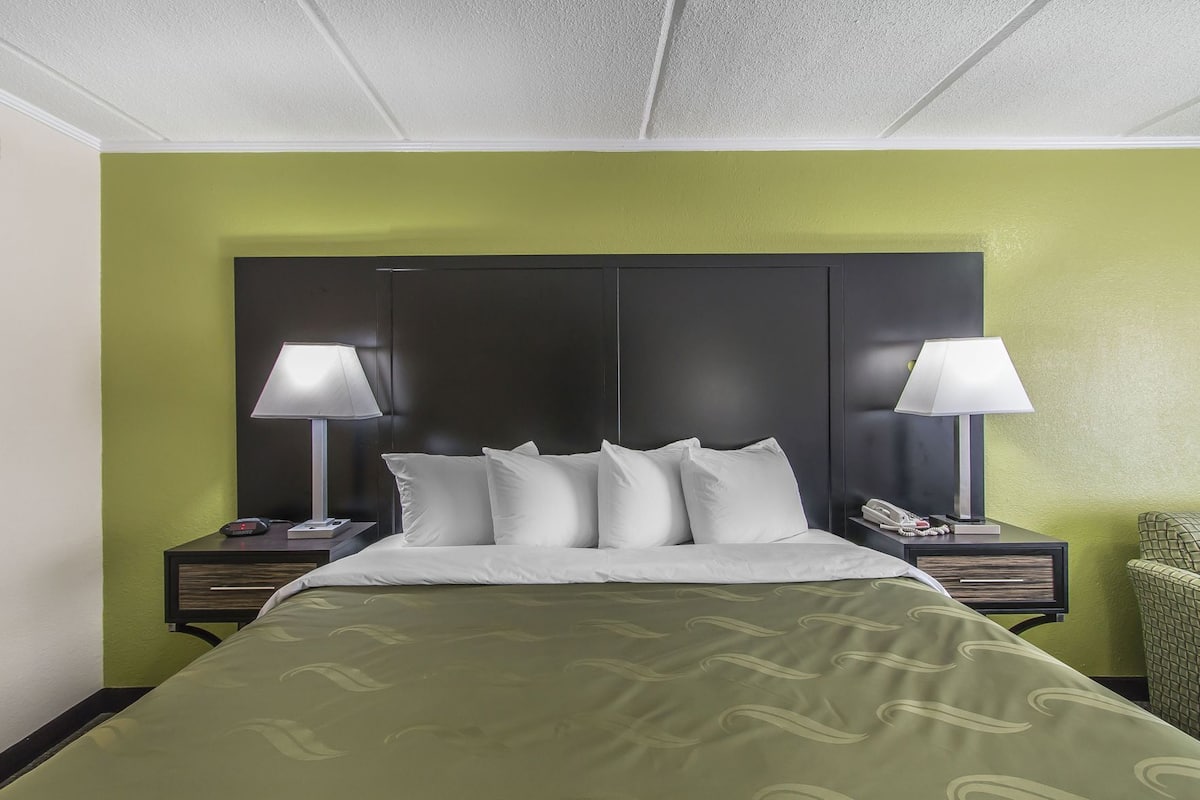 A hotel room with a bed, two bedside tables with lamps, a telephone, and a green wall.