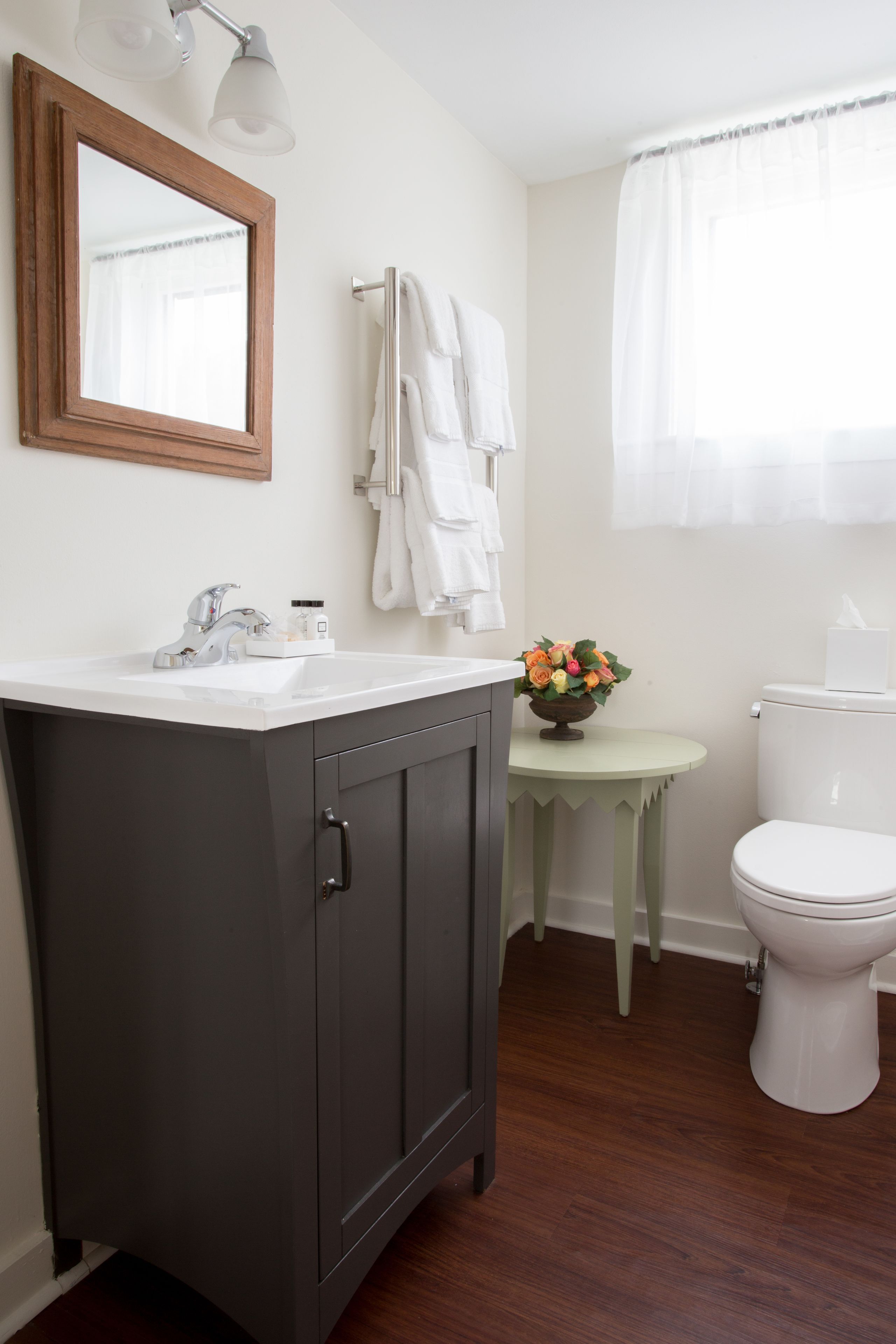A bathroom with a dark wooden vanity, a white sink, a mirror, a toilet, and a small round table with a vase of flowers.