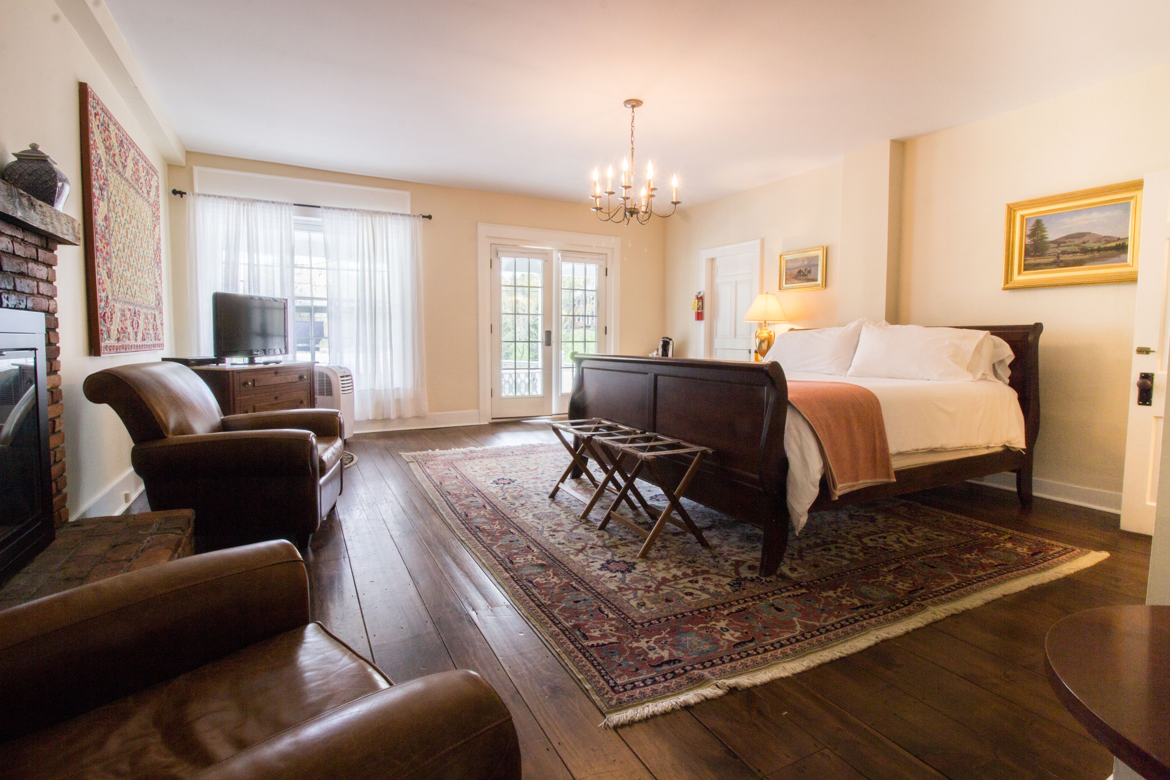 Une chambre d’hôtel équipée d’un lit, d’une télévision, d’une cheminée, de fauteuils en cuir et d’un grand tapis.