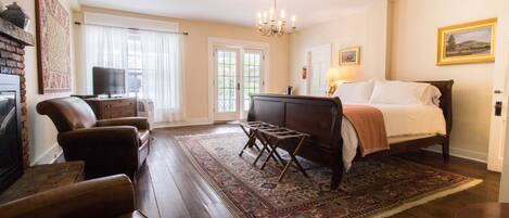 Une chambre d’hôtel équipée d’un lit, d’une télévision, d’une cheminée, de fauteuils en cuir et d’un grand tapis.