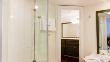 Un baño moderno con ducha de vidrio, piso de madera y lavamanos blanco con espejo.