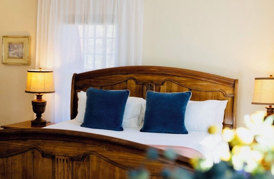 A neatly made bed with a wooden headboard, two blue pillows, and white bedding.