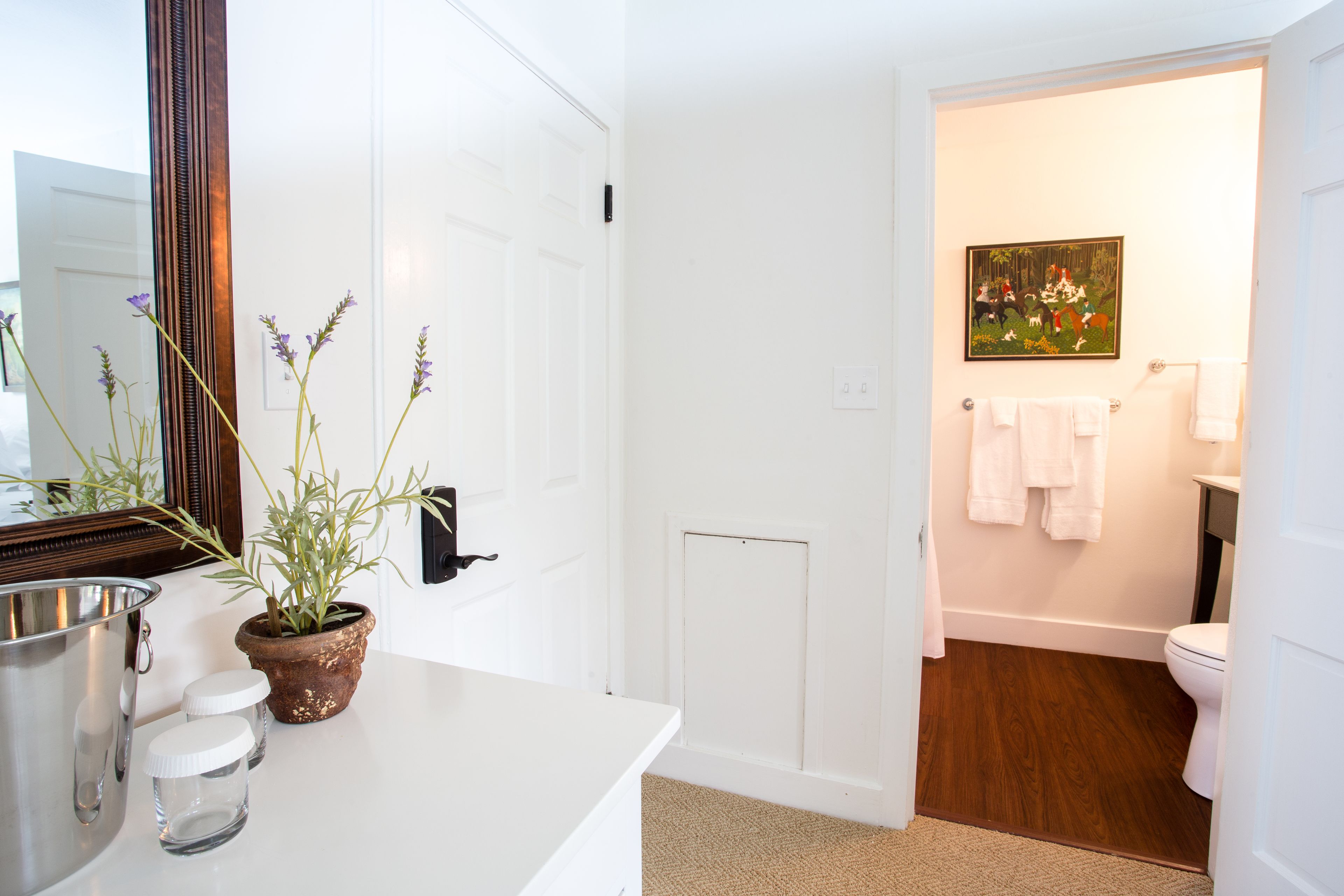 A bathroom with a white sink, a mirror, a potted plant, and a painting on the wall.