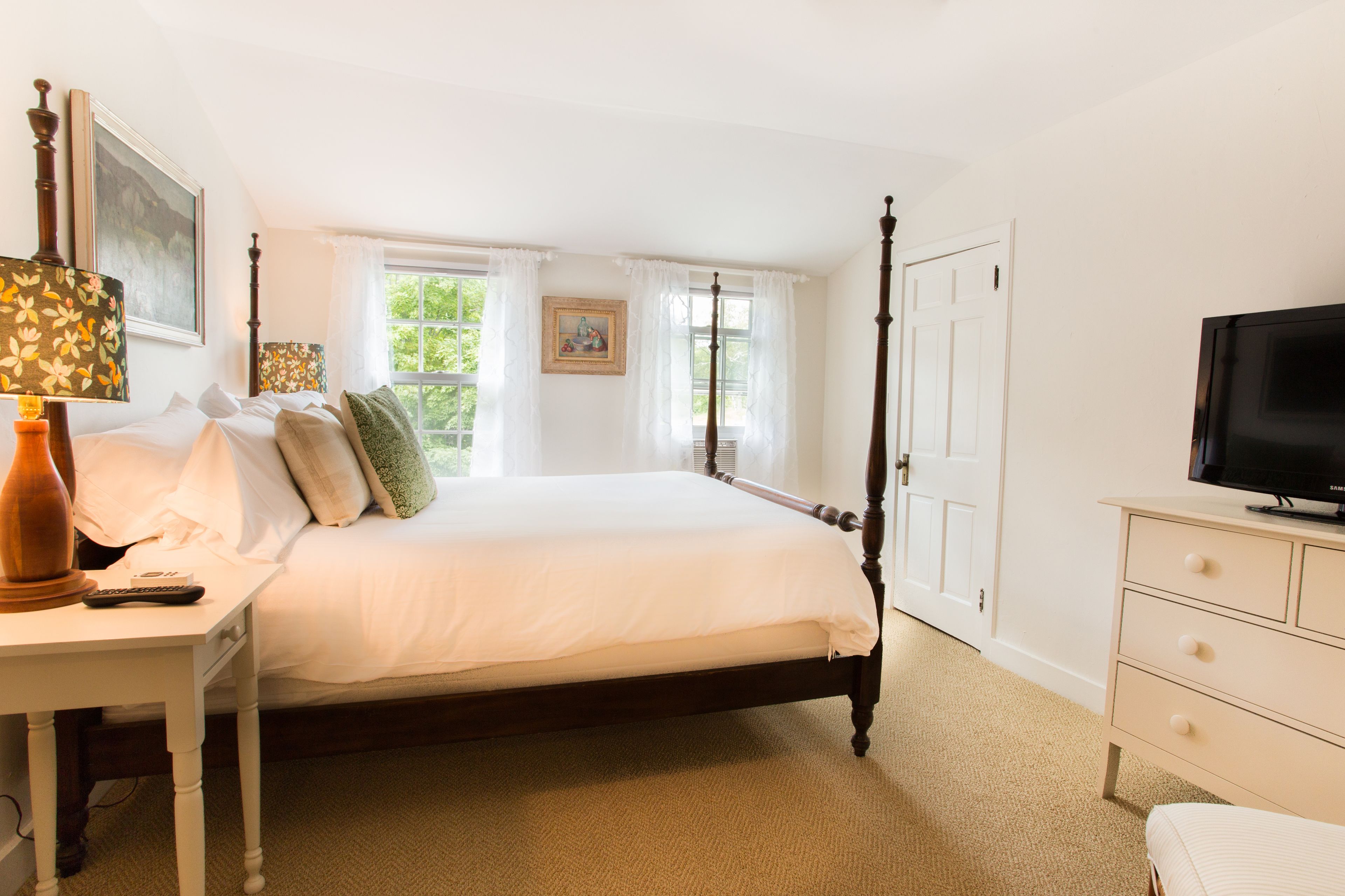 Een slaapkamer met een hemelbed, nachtkastje met lamp, een dressoir en een televisie.