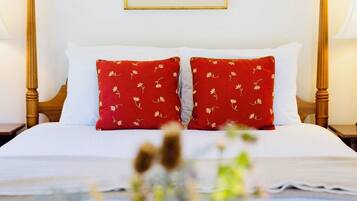 Un lit bien fait, orné d’oreillers blancs et rouges, un tableau encadré accroché au mur et un vase rempli de fleurs posé sur la table de chevet.